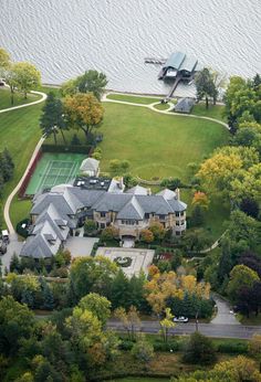 an aerial view of a large house with tennis court in the foreground and trees surrounding it