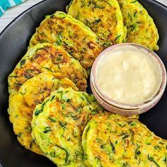 zucchini fritters on a black plate with a bowl of dip