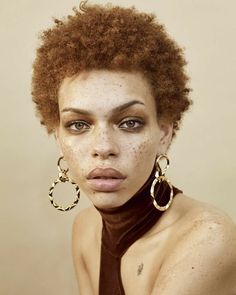 a woman with freckles on her face wearing gold hoop earrings and a brown top