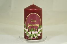 a red candle with white flowers and green leaves on the top, sitting in front of a white background