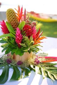 an arrangement of tropical flowers and greenery is displayed on a table at a wedding