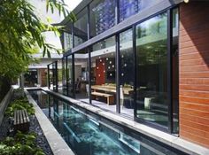 an outdoor swimming pool in front of a house with glass walls and sliding doors on the side