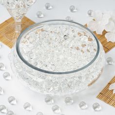 a glass bowl filled with water next to two vases and some white flowers on a table