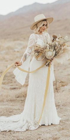 a woman in a white dress and hat holding a bouquet of dried flowers on the desert