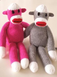 two knitted sock monkeys sitting next to each other on a white surface with pink and grey colors