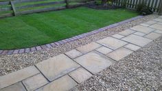 a brick walkway in the middle of a garden with green grass and wooden fence behind it