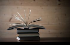 an open book sitting on top of two stacked books next to each other in front of a wooden wall