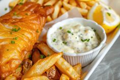 fish and fries on a plate with a small bowl of sauce