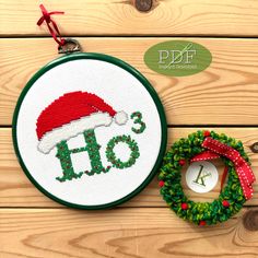 a cross stitch christmas ornament with a santa hat on it, next to a wreath