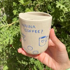 a hand holding a coffee cup with the words wanna coffee? on it in blue ink