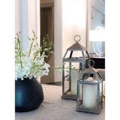 two metal lanterns sitting on top of a table next to a vase filled with flowers