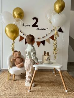 a little boy standing in front of a birthday cake and balloons with the number two on it