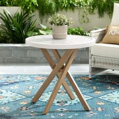 a small white table sitting on top of a blue rug next to a chair and potted plant