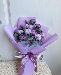 a bouquet of crocheted flowers is wrapped in purple paper and tied with a ribbon