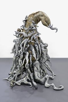 a sculpture made out of silver and gold colored metal parts on a gray surface with a white wall in the background