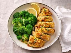 a white plate topped with chicken, broccoli and lemon wedges on top of a table