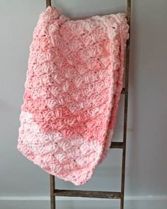 a pink crocheted blanket hanging on a ladder