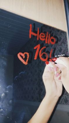 a person writing on a sign that says hello to us with red ink and hearts