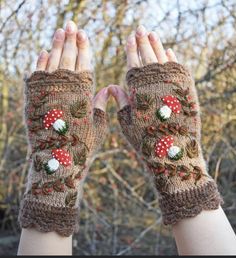 two hands wearing knitted mittens with flowers and berries on them, one is holding the other