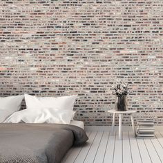 a bed sitting in front of a brick wall next to a table with flowers on it