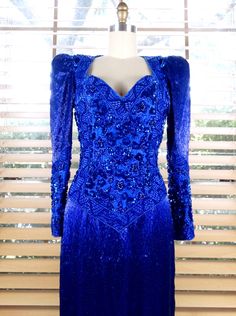 "A beautiful vintage gown HEAVILY embellished with bright blue glass beading, faux blue pearls and sequins. It's in excellent condition! ✤ Tag Size - Small ✤ Bust - 32/34\" (padded chest) ✤ Waist - 25\" ✤ Hips - 35\" ✤ Shoulders - 15\" ✤ Sleeves - 23\" ✤ Total Length - 57\" This dress comes from a pet-free and smoke-free home. If you would like more info or have any questions, please don't hesitate to ask!" Blue Beaded Evening Dress For Prom, Blue Beaded Evening Dress For Wedding, Blue Beaded Wedding Evening Dress, Blue Embellished Gown For Cocktail, Embellished Blue Cocktail Gown, Blue Embellished Cocktail Gown, Blue Beaded Floor-length Evening Dress, Cocktail Embellished Blue Gown, Fitted Royal Blue Embellished Gown