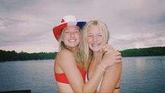 two young women hugging each other by the water