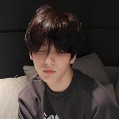 a young man sitting on top of a couch next to a white pillow with his eyes closed