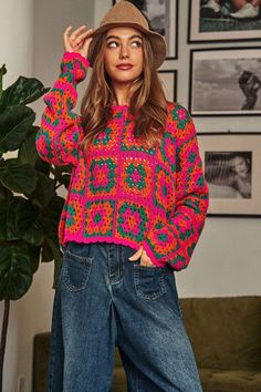 a woman standing in front of a green couch wearing a hat and colorful knitted sweater