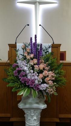 a large bouquet of flowers sitting on top of a white pedestal in front of a cross