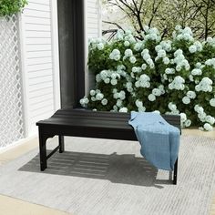 a black bench sitting on top of a rug in front of a white fence and bushes