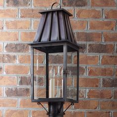 an old fashioned lantern hanging on the side of a brick wall with three candles in it