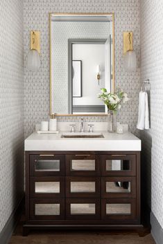 a bathroom vanity with two sinks and a large mirror above it, in front of a patterned wallpapered wall