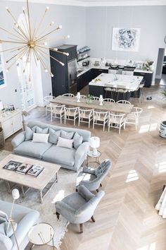 an aerial view of a living room and dining room with wood floors, gray couches, white chairs, gold chandelier