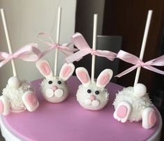 four cake pops decorated with bunny ears and white frosting on a pink tablecloth