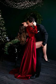 a man and woman kissing in front of a christmas tree with lights hanging from the ceiling