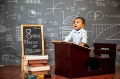 a baby sitting at a podium in front of a chalkboard