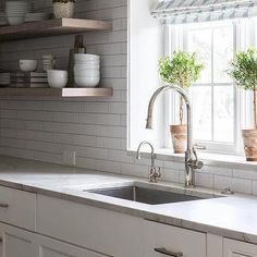 a kitchen with white cabinets and open shelving above the sink is decorated with potted plants