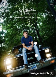 a young man sitting on the hood of a pickup truck with trees in the background