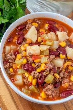 a white bowl filled with chili and corn next to a spoon on a wooden table