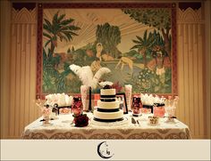 a table topped with a white and black cake next to a large painting on the wall