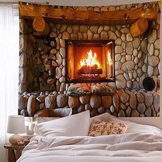 a bed with pillows and blankets in front of a fire place that is made out of rocks