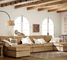 a living room filled with lots of furniture next to two large windows and wooden beams