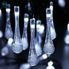 several clear glass vases hanging from a string with lights in the back ground behind them