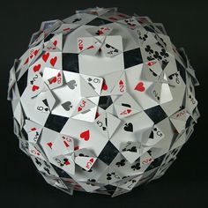 an origami ball with playing cards cut out of it, on a black background