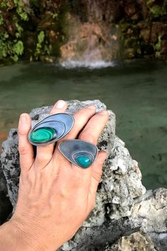 Two rings on a hand with a waterfall in the background. The rings are oversized and statement, both with tops that reach over the top of the neighboring fingers. one features a malachite and the other a chrysocolla Art Rings, Chrysocolla Ring, Bold Art, Statement Art, Vibrant Blue, Free Spirit, Peru