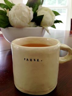 a coffee mug sitting on top of a wooden table next to a vase with flowers