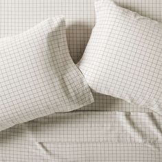 two white pillows sitting on top of a bed covered in sheets and pillowcases