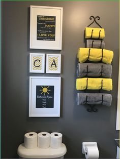 a bathroom with yellow towels hanging on the wall next to toilet paper rolls and pictures