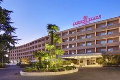 the crowne plaza hotel is lit up at night with palm trees in front of it