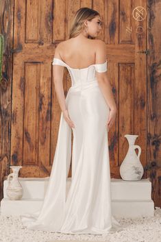 a woman in a white wedding dress standing next to a wooden door with her back turned